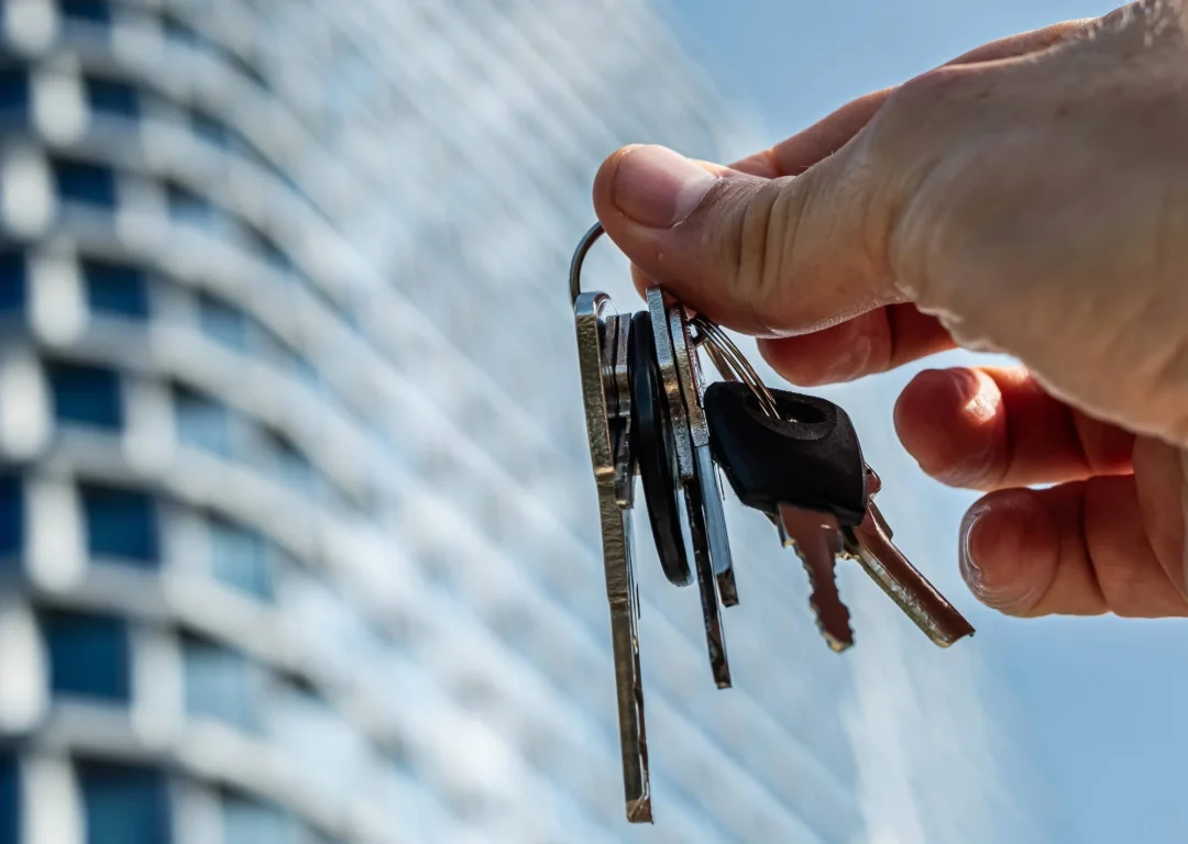 A hand holding keys in front of a large office building.