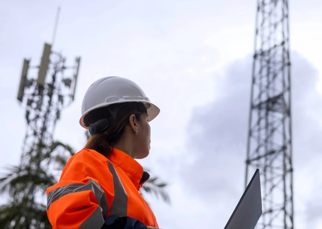 A woman in protective gear looks at a telecoms mast.
