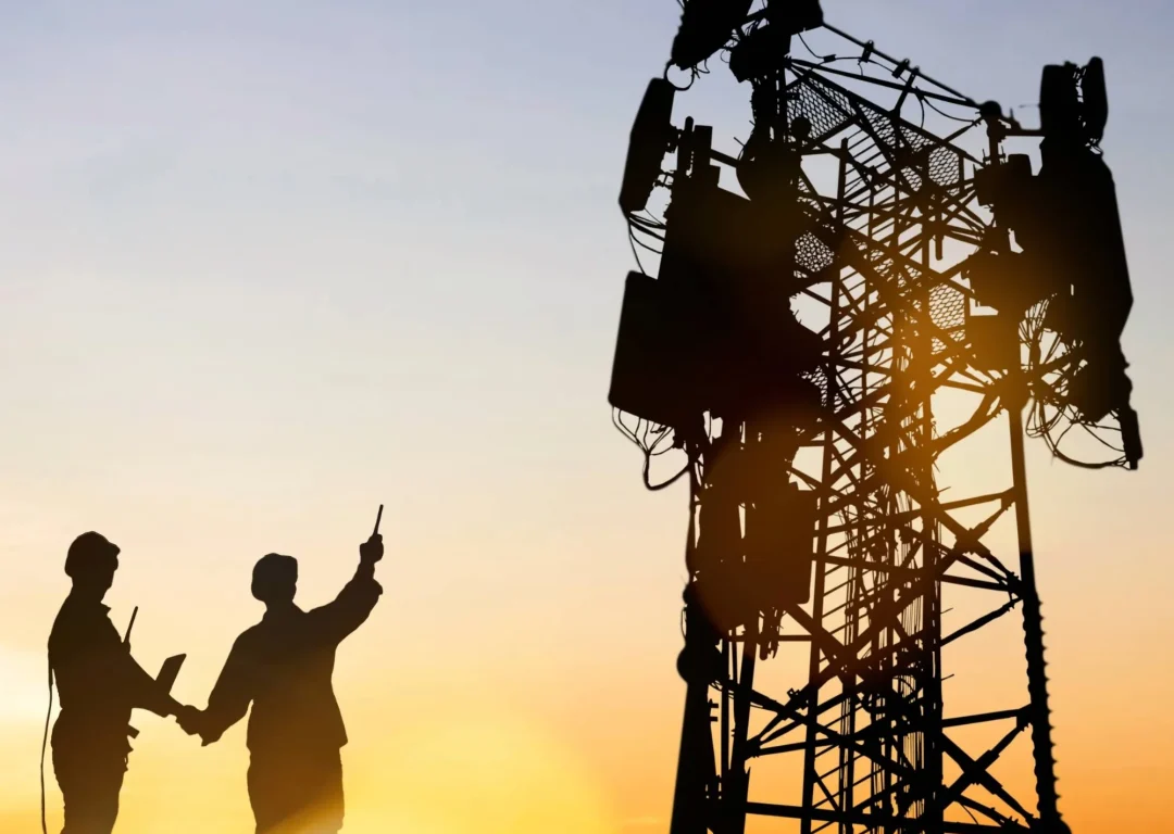 Two silhouetted people stand in front of a large telecoms mast.