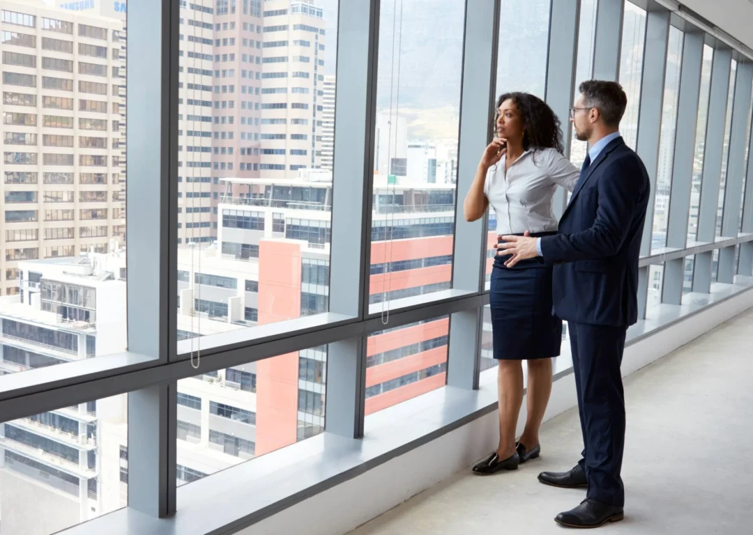 Two business professionals looking out the window of an office building.